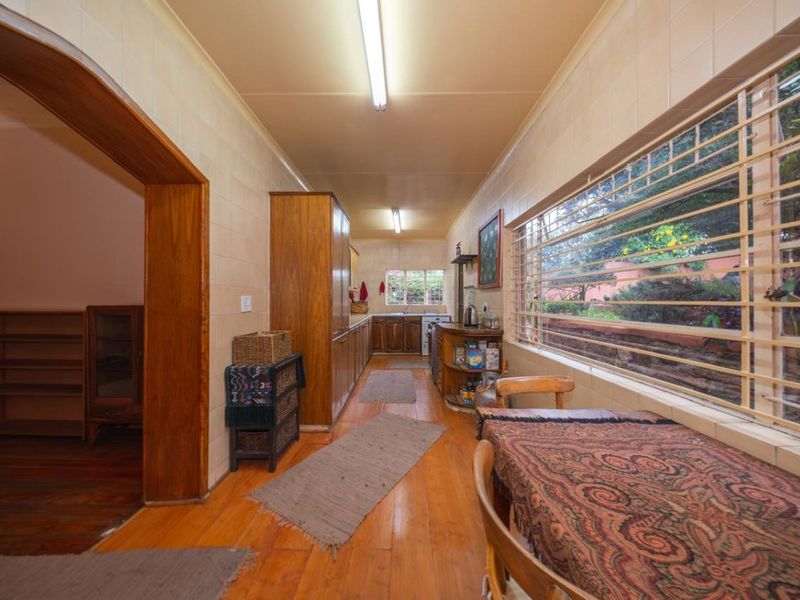 A galley-style kitchen featuring wooden cabinetry, tiled walls, and hardwood flooring, with large windows fitted with security bars.
