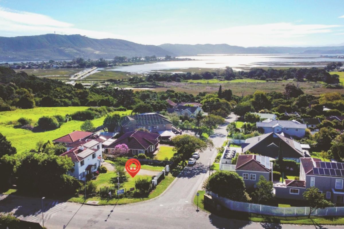Aerial view of a residential neighbourhood featuring houses with tiled roofs, solar panels, and surrounding green landscapes with distant water views.