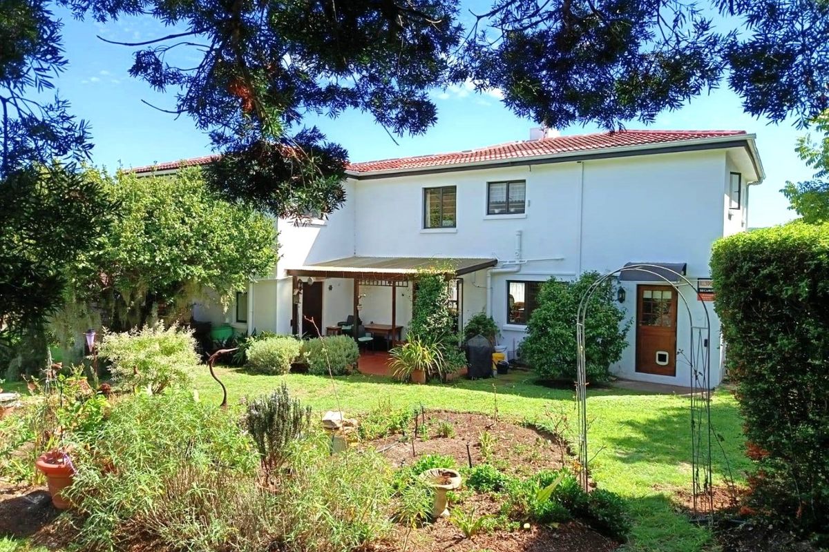 Rear view of the property featuring a landscaped garden, lawn area, and a covered patio attached to the main building structure.