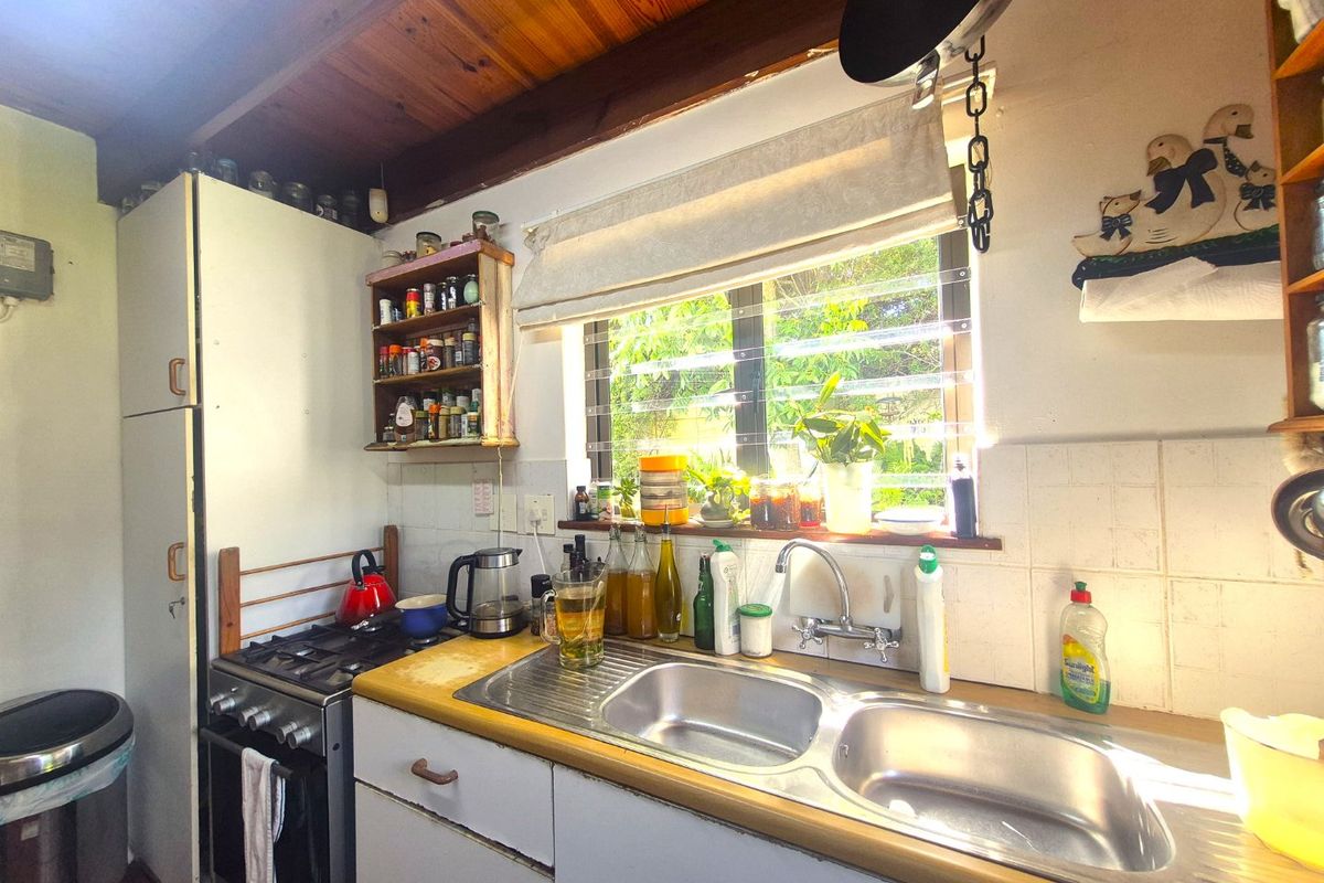 A compact kitchen featuring a double stainless steel sink, gas stove, and exposed timber ceiling beams, offering a functional but dated workspace.
