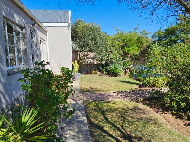 A view of the rear garden featuring a brick paved pathway, established landscaping, and the side elevation of the house with casement windows.