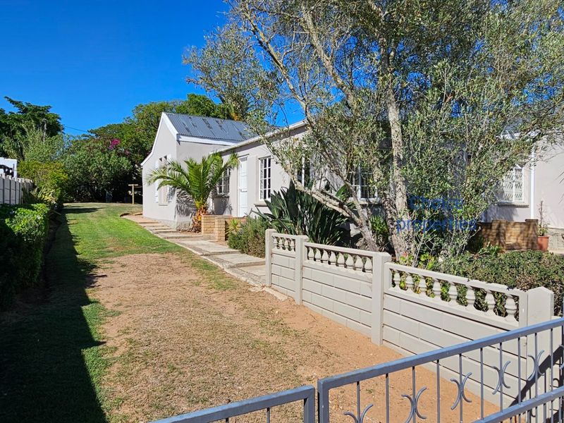 Front exterior view of the house featuring a paved walkway, established garden, and secure boundary walling with a metal gate.