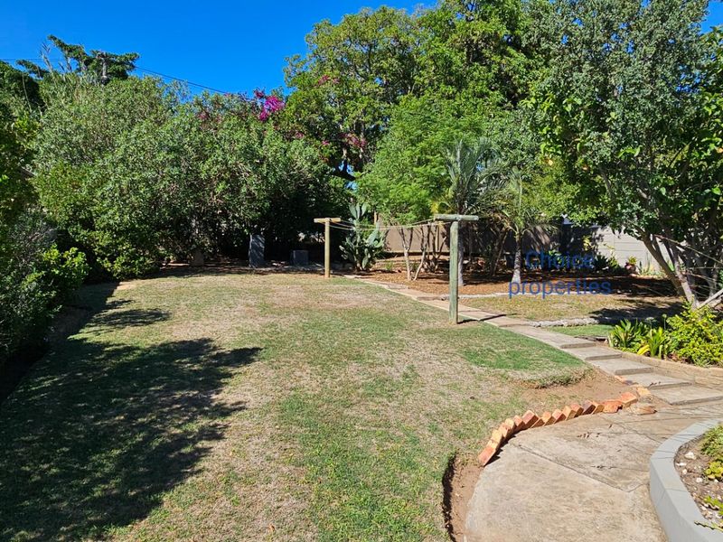A spacious backyard garden featuring a lawn, mature trees, a paved pathway, and a rainwater collection tank.