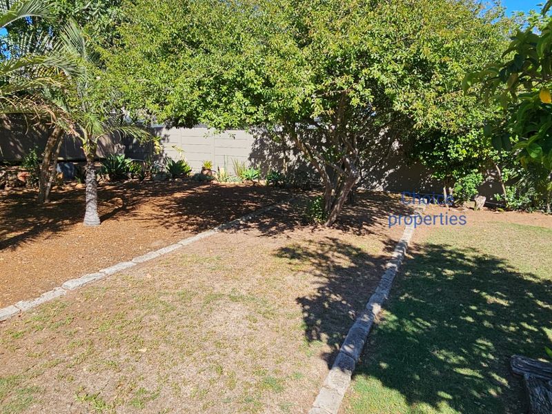 A private garden area featuring mature trees, established landscaping, and stone-edged lawn borders enclosed by a boundary wall.