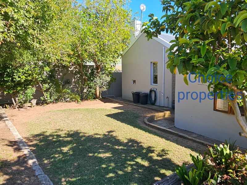 A private rear garden featuring a well-maintained lawn, established trees, and stone-edged garden beds adjacent to the property's exterior wall.
