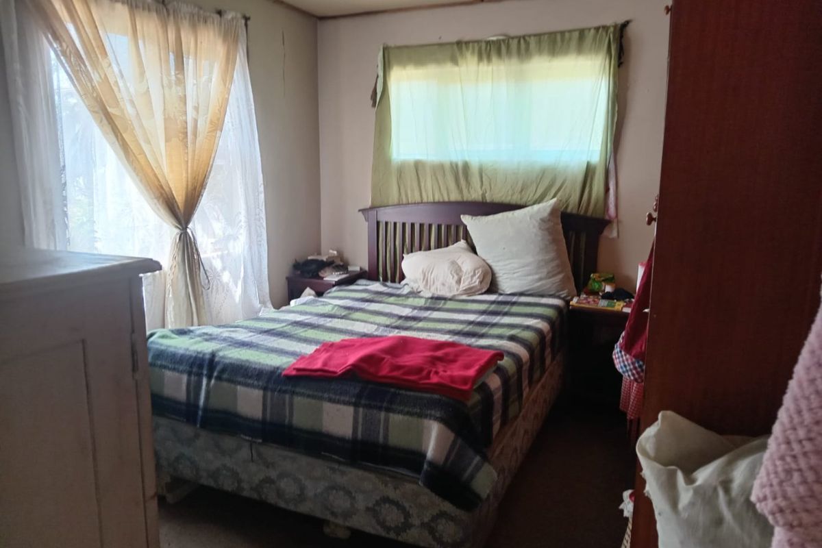 A bedroom featuring standard window fixtures and dated wall and ceiling finishes, requiring cosmetic updates to improve the overall aesthetic.