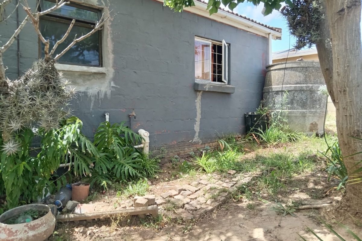 Rear exterior view of the property featuring a grey painted wall, security window bars, an external water tank, and a small paved garden area.