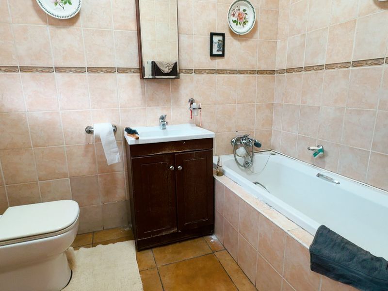 A dated bathroom featuring full-height wall tiling, a built-in bathtub, a toilet, and a vanity cabinet with visible wear.