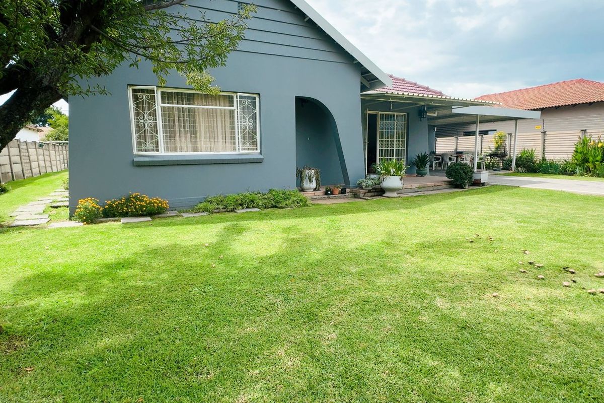 Rear view of the house featuring a well-maintained lawn, a covered patio area, and a paved driveway leading to the side of the property.