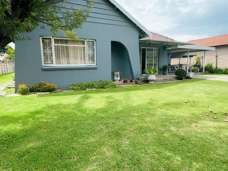 Rear view of the house featuring a well-maintained lawn, a covered patio area, and a paved driveway leading to the side of the property.