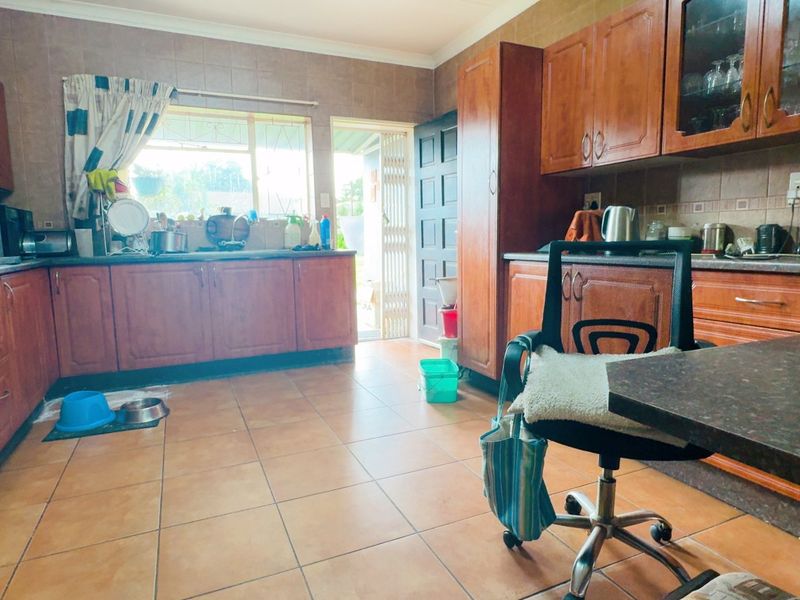 A functional kitchen featuring extensive wooden cabinetry, tiled flooring, and a tiled backsplash, offering a traditional layout with direct access to the exterior.