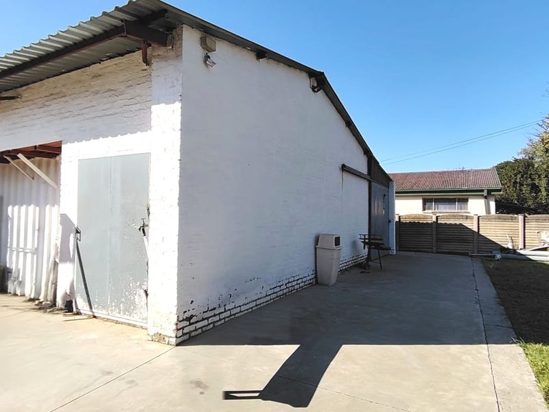 Rear exterior view of a utility building featuring a concrete paved area, painted brick walls, and a metal roof structure.