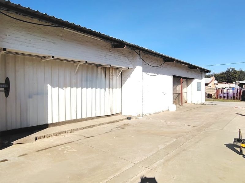 Rear exterior view of the property featuring a large concrete driveway, painted brick walls, and corrugated metal roofing.