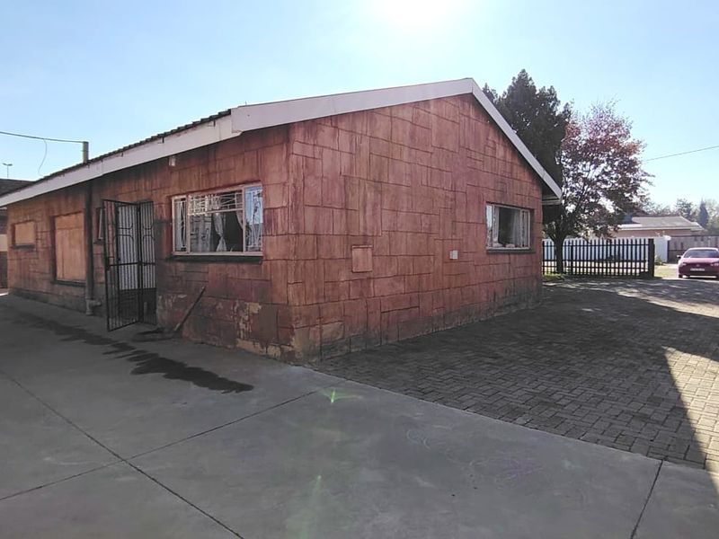 Exterior view of a detached house featuring a paved driveway, security gate, and weathered masonry walls with some windows boarded up.