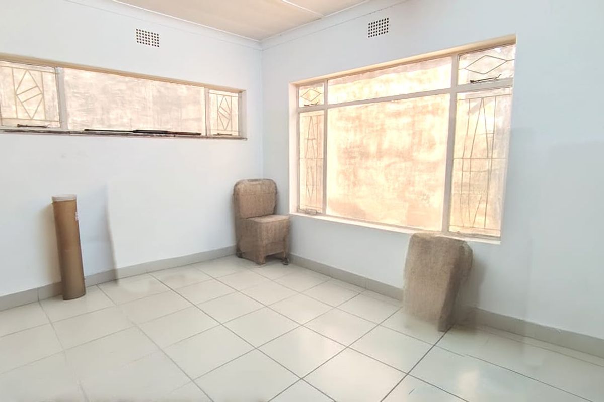 A bright, empty living room featuring tiled flooring and large windows with security bars, offering a blank canvas for potential renovation.