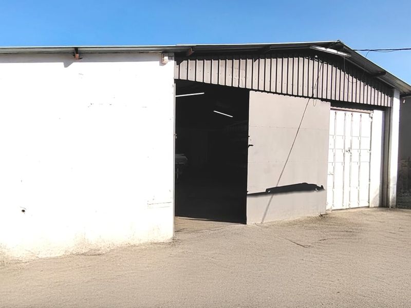 A functional garage structure featuring a large sliding metal door and corrugated roofing, situated on a concrete apron.