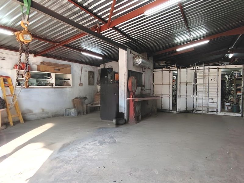 Spacious industrial-style garage featuring exposed steel roof trusses, concrete flooring, and integrated shipping containers for additional storage or workspace utility.