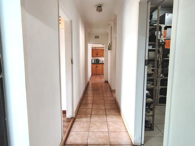 A functional hallway with tiled flooring connecting multiple rooms, leading towards a kitchen area at the end.