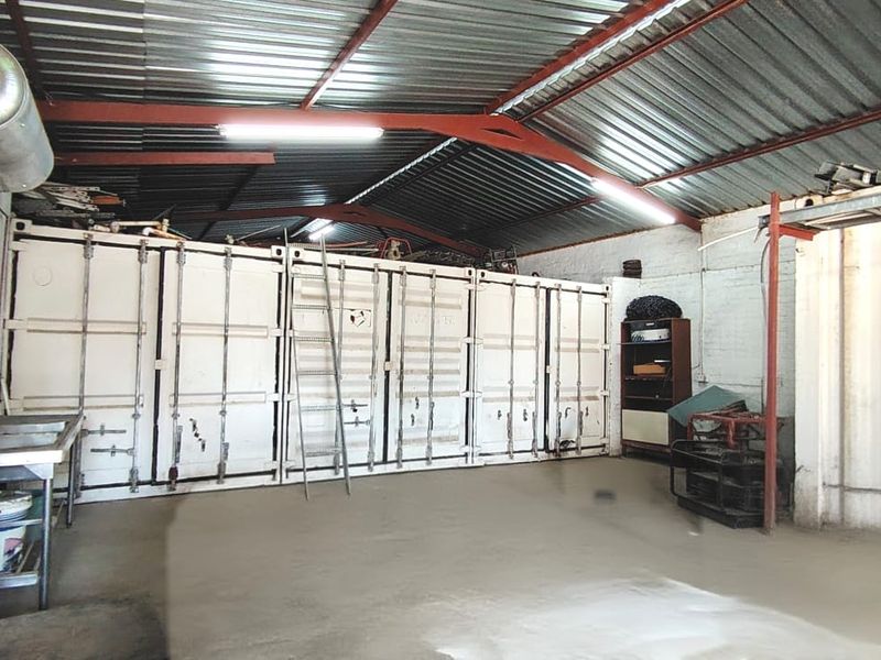 A spacious utility area featuring concrete flooring, exposed steel roof trusses, a stainless steel sink, and an electric water heater, suitable for workshop or storage.