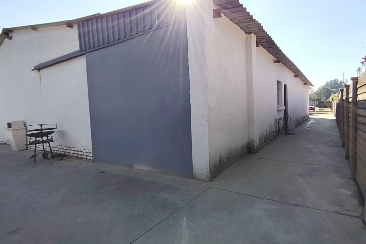 Rear exterior view of the property showing concrete paving, boundary wall, and building facade with visible signs of wear and maintenance requirements.