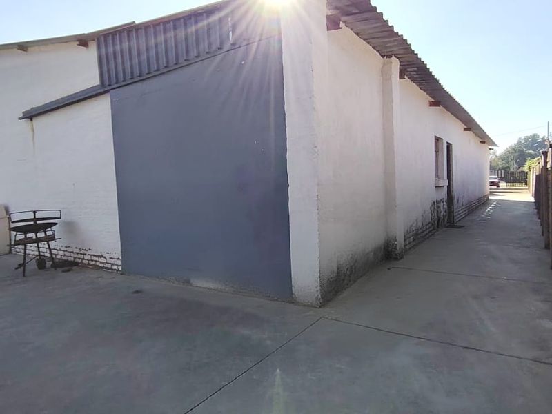 Rear exterior view of the property showing concrete paving, boundary wall, and building facade with visible signs of wear and maintenance requirements.
