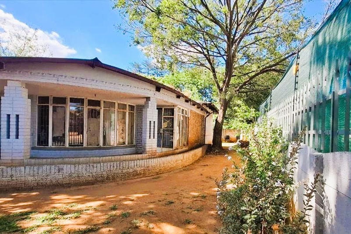 Rear exterior view of the property featuring a curved veranda, large windows, and a brick boundary wall with security fencing.
