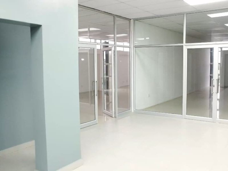 A bright, open-plan commercial office space featuring modern glass partitions, tiled flooring, and a clean drop ceiling with recessed lighting.