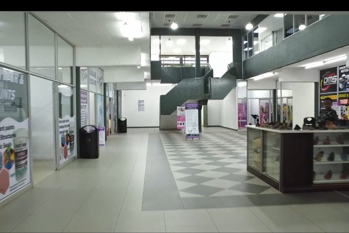A spacious commercial hallway featuring tiled flooring, glass partitions, and a central staircase leading to an upper level.