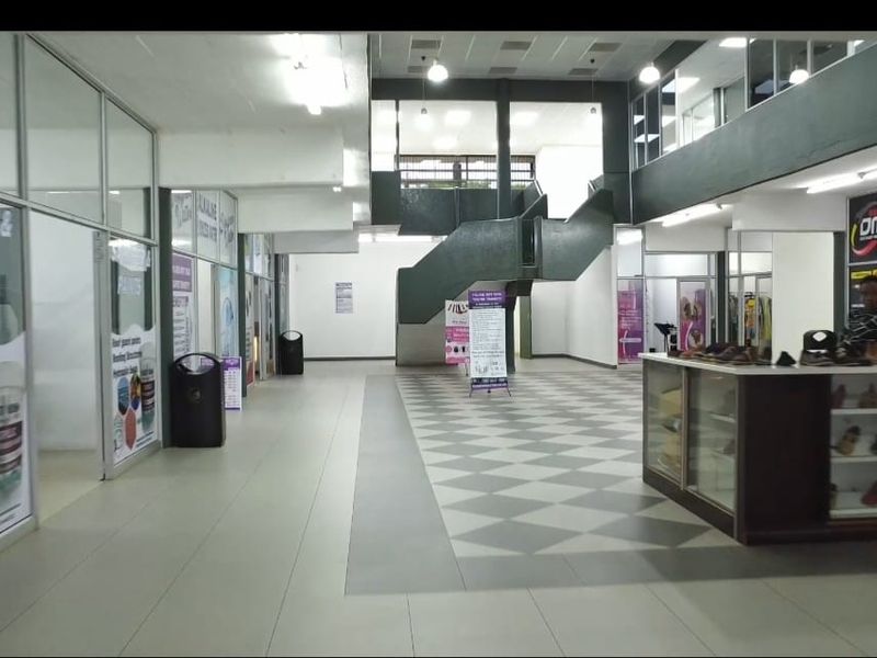 A spacious commercial hallway featuring tiled flooring, glass partitions, and a central staircase leading to an upper level.