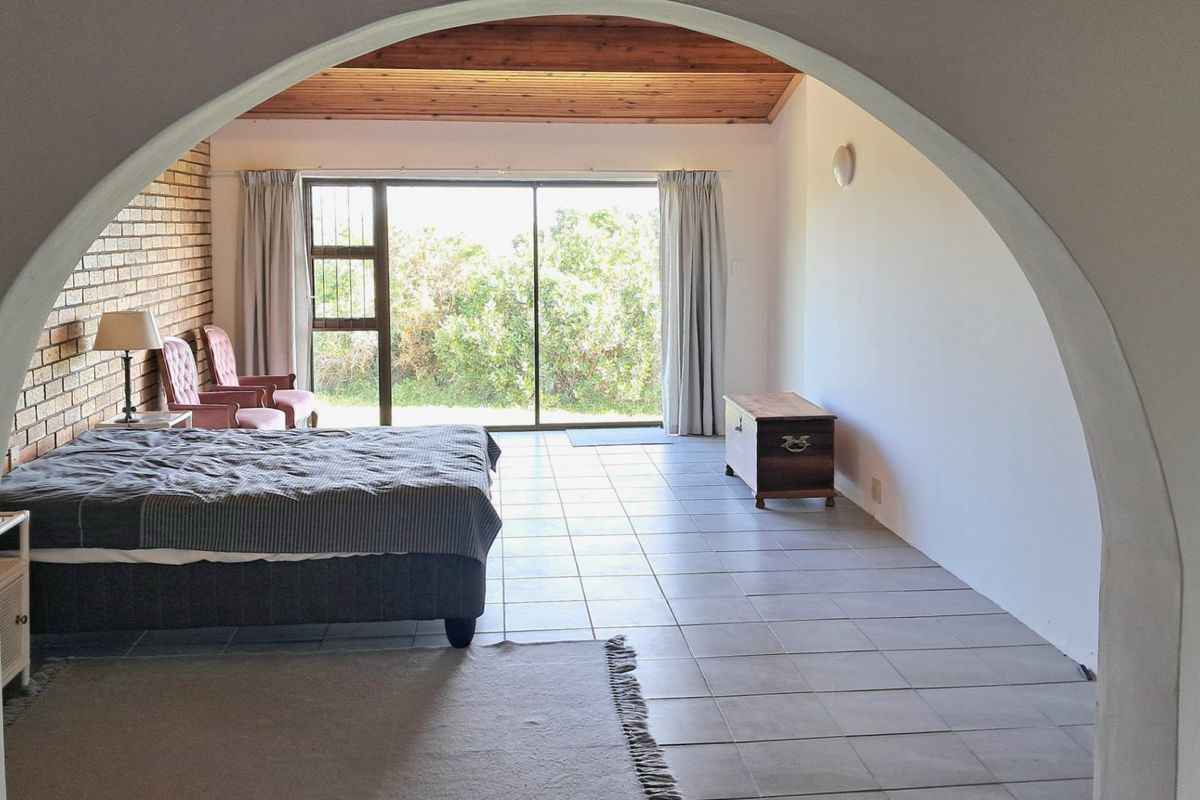 Spacious bedroom featuring an exposed brick wall, timber ceiling, tiled flooring, and large sliding glass doors providing natural light and garden access.