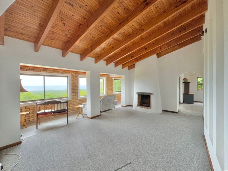 Spacious living room featuring a vaulted timber beam ceiling, a unique built-in fireplace, and large windows showcasing scenic landscape views.