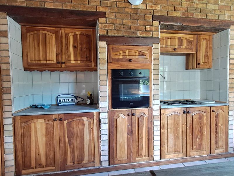 A rustic kitchen featuring solid wood cabinetry, a brick feature wall, built-in oven, and gas hob with tiled backsplash.