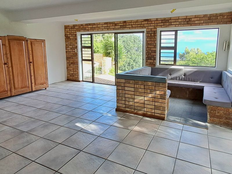 Spacious living area featuring exposed brick walls, tiled flooring, and a unique built-in brick seating nook with expansive views through large windows.