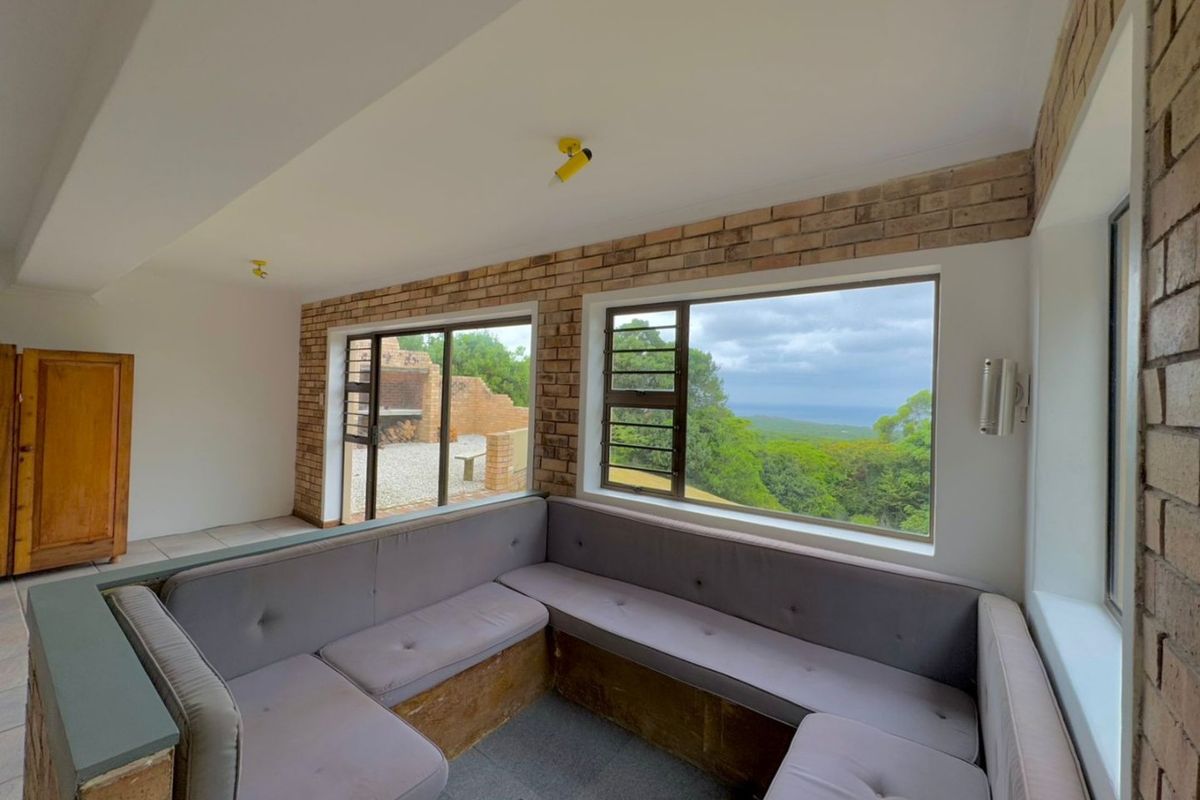 Living area featuring built-in seating, exposed brick walls, and large windows offering scenic landscape views with access to an outdoor patio area.