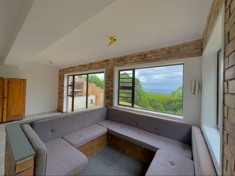Living area featuring built-in seating, exposed brick walls, and large windows offering scenic landscape views with access to an outdoor patio area.