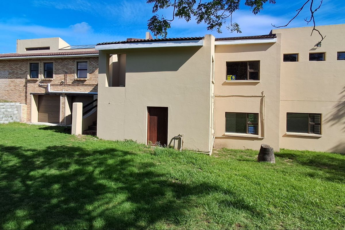 Rear view of the farm property showing a mix of brick and plastered exterior walls, aluminium windows, and a surrounding lawn area.