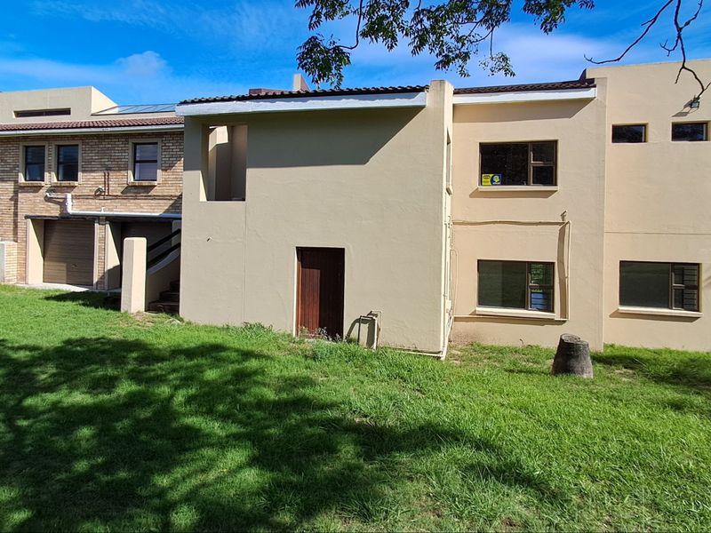 Rear view of the farm property showing a mix of brick and plastered exterior walls, aluminium windows, and a surrounding lawn area.