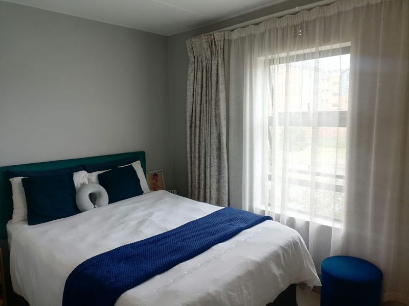 A well-maintained bedroom featuring neutral wall tones and a large window with layered curtains, providing natural light to the space.