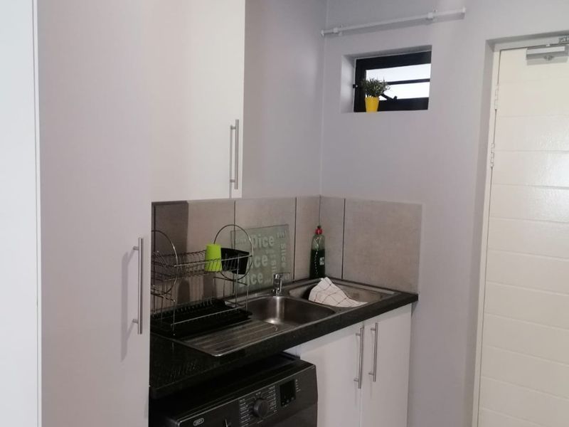 A functional laundry area featuring built-in white cabinetry, a stainless steel sink with granite countertop, tiled backsplash, and tiled flooring.