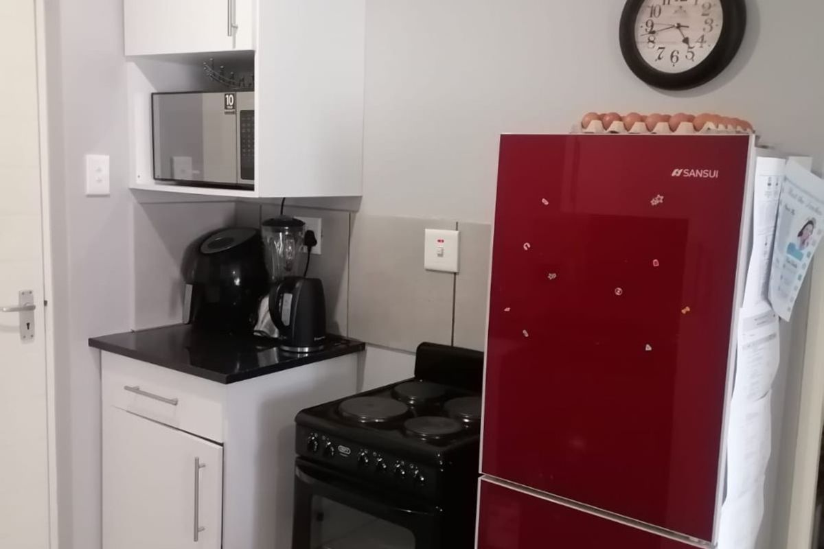 A compact kitchen area featuring white cabinetry, black stone countertops, tiled splashbacks, and tiled flooring, providing a functional and clean workspace.