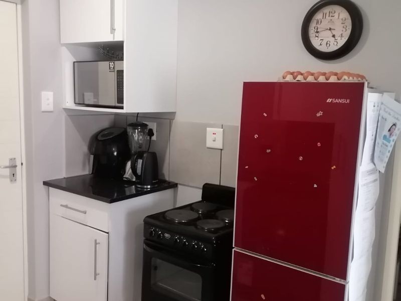 A compact kitchen area featuring white cabinetry, black stone countertops, tiled splashbacks, and tiled flooring, providing a functional and clean workspace.