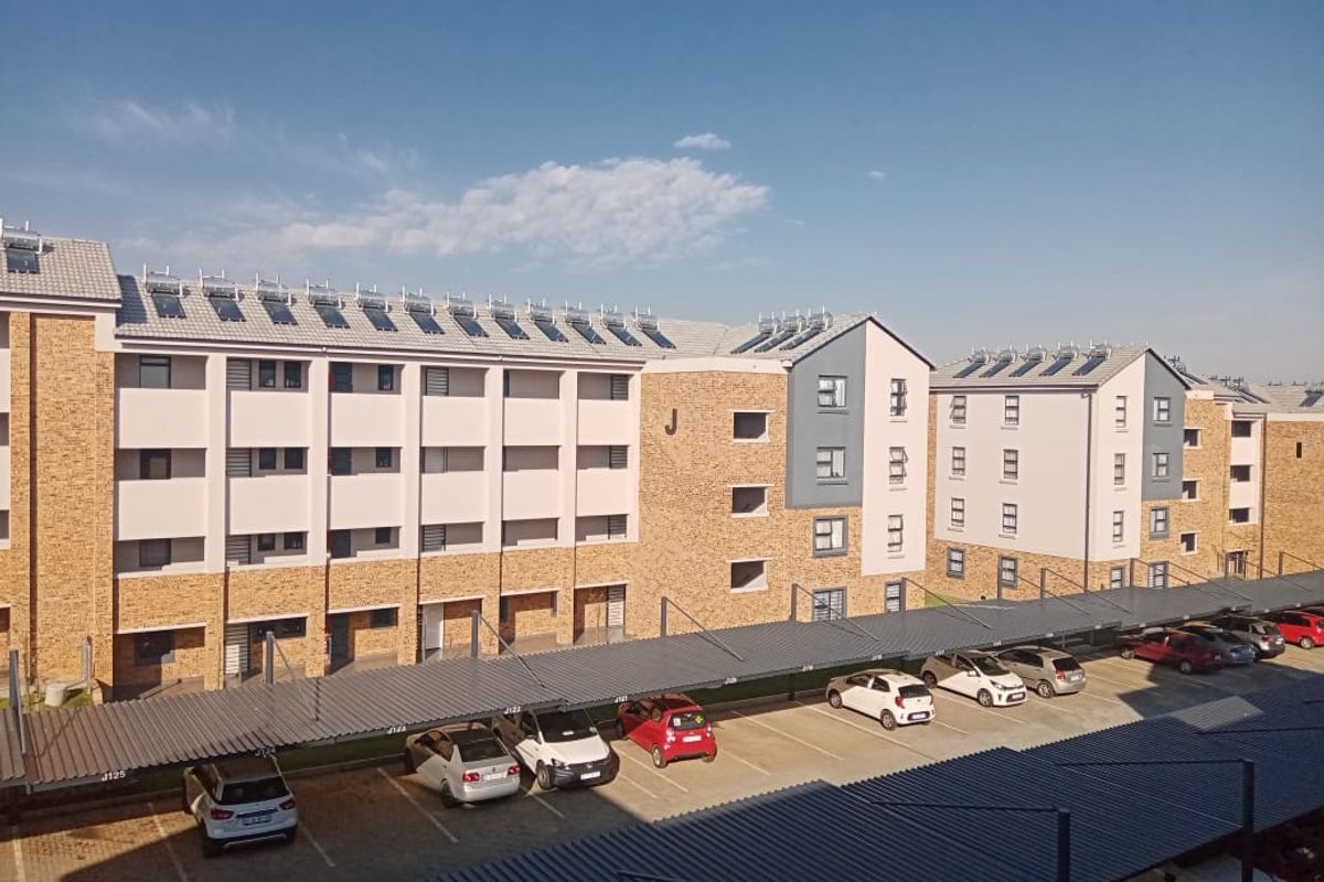Exterior view of a multi-story apartment complex featuring facebrick architecture, solar water heating panels, and designated covered parking bays.