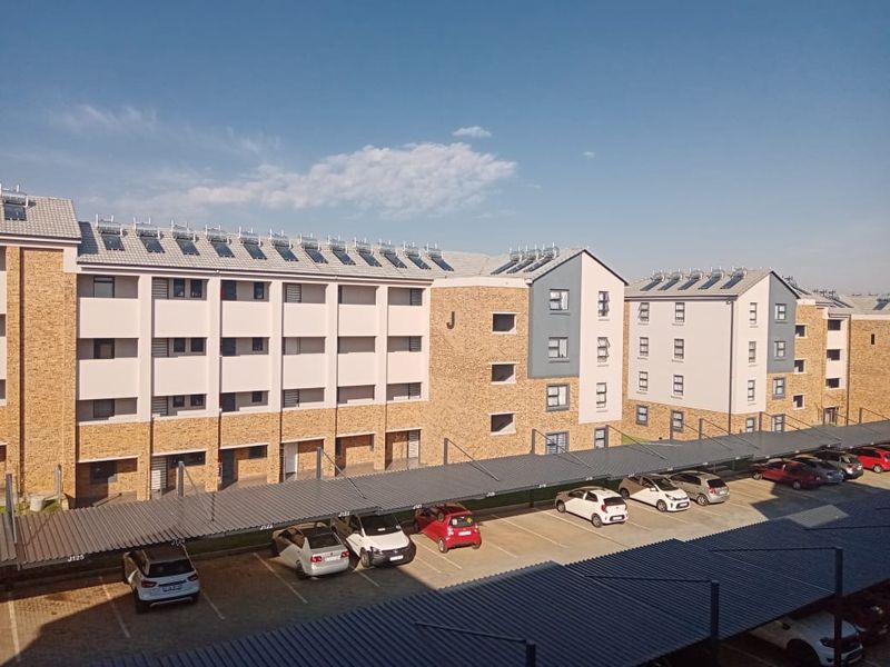 Exterior view of a multi-story apartment complex featuring facebrick architecture, solar water heating panels, and designated covered parking bays.