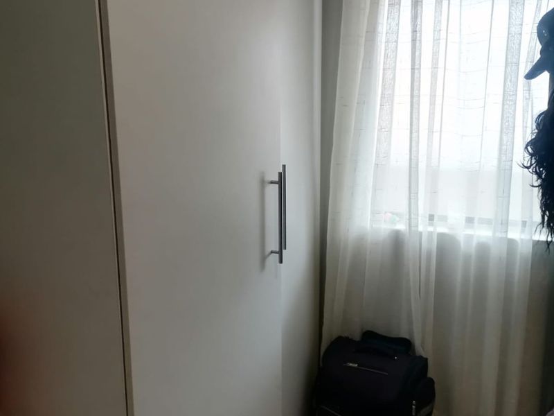 A bedroom featuring a modern white built-in wardrobe and tiled flooring, positioned next to a window with sheer curtains.