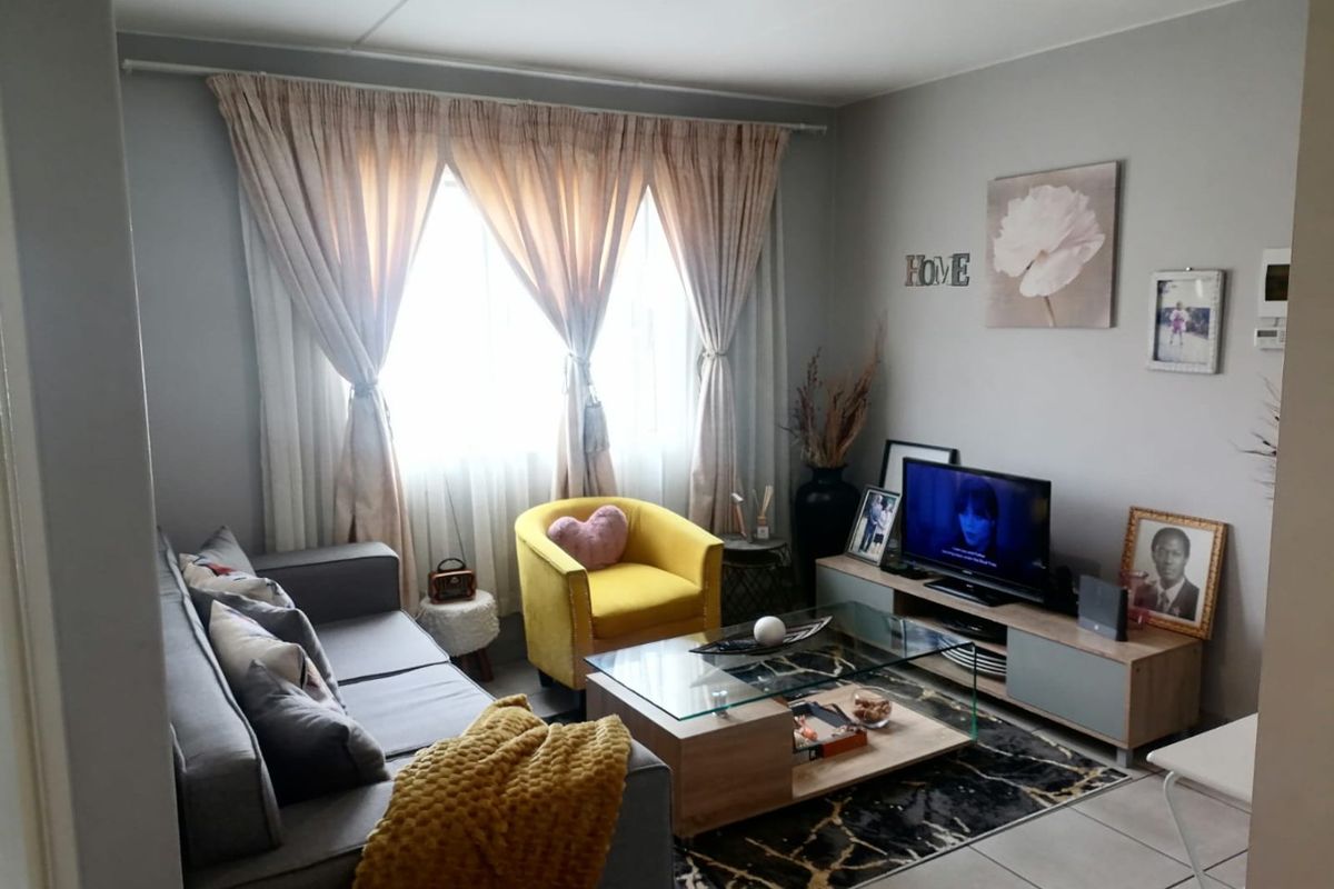 A comfortable living room featuring tiled flooring and large windows with curtain tracks, providing a functional and well-lit space for relaxation.