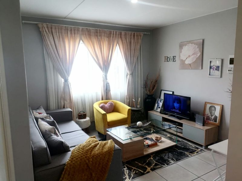 A comfortable living room featuring tiled flooring and large windows with curtain tracks, providing a functional and well-lit space for relaxation.