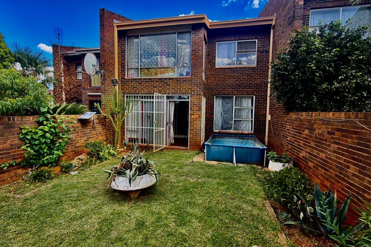 Rear view of a brick townhouse featuring a private garden, security gate, and sliding door access to the main living area.