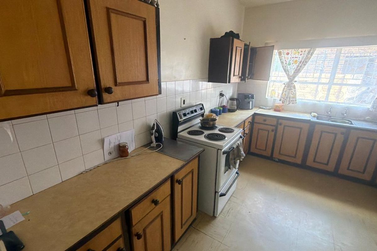 A functional kitchen featuring traditional wooden cabinetry, laminate countertops, a tiled backsplash, and a freestanding electric stove with a window view.