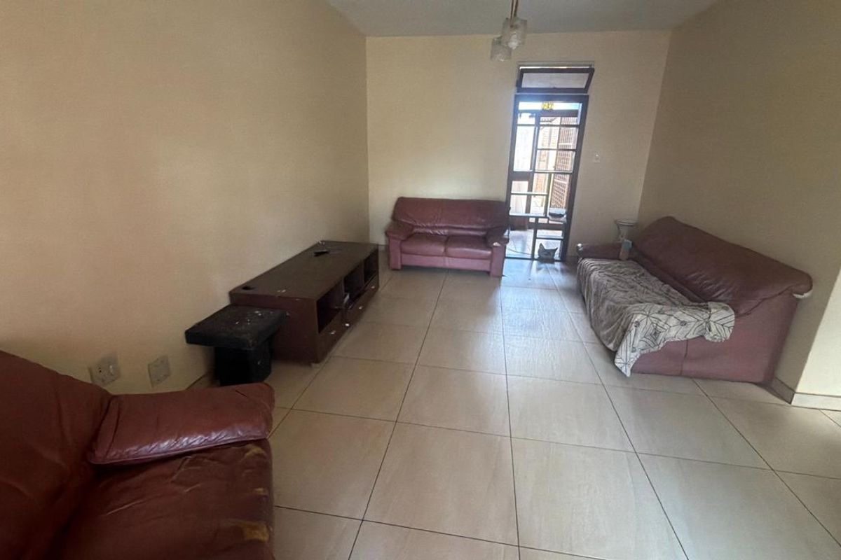 A spacious living room featuring neutral tiled flooring and a glass panel door providing access to the exterior.