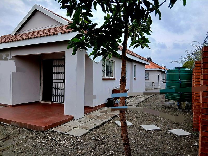 Rear view of the house featuring a covered patio, paved walkway, and a water storage tank set within an unlandscaped garden area.